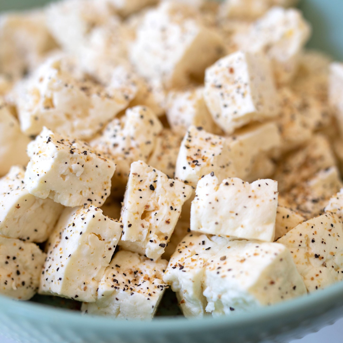 Cubed tofu with seasoning in a teal bowl on a light background